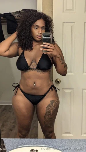 Woman with curly hair in black bikini taking mirror selfie in bathroom.