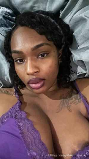 Woman with curly hair in purple lace lingerie lying on gray sheets.