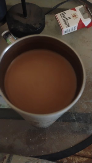 No person. Mug of brown liquid on table with cigarette pack.