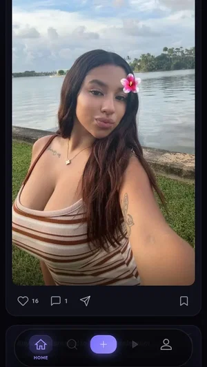 Woman with long dark hair and flower in hair, wearing striped top, outdoors near water.