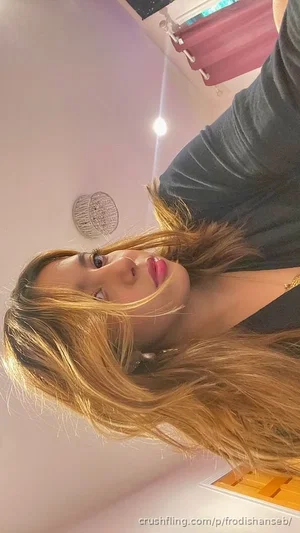 Woman with long blonde hair in dark top, indoors, looking at camera.
