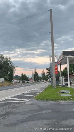 Gas station with digital price sign, road, and overcast sky.