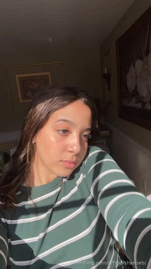 Woman with long dark hair in green and white striped shirt, taking indoor selfie.