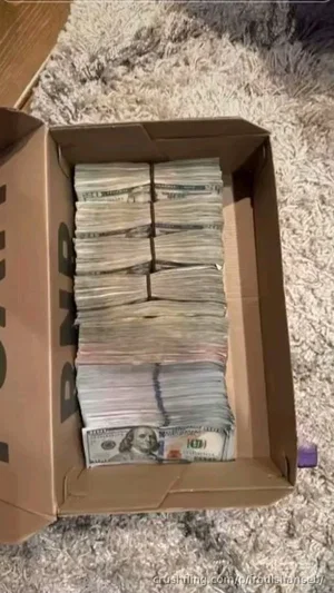 Box filled with stacks of US $100 bills on a shaggy carpet.
