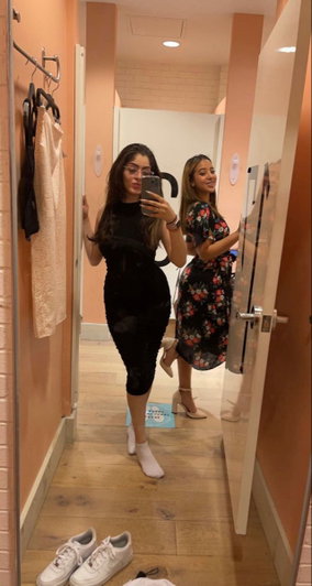 Two women in dresses taking a mirror selfie in a hallway.