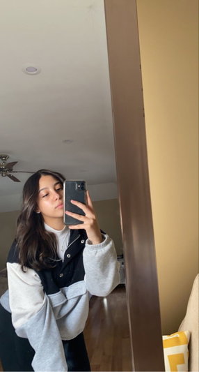 Woman with long dark hair taking mirror selfie in sweatshirt indoors.
