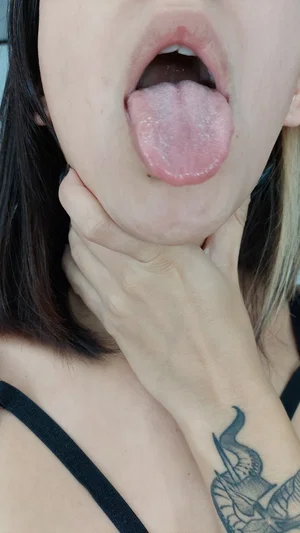 Woman with dark hair and tattooed hand sticks tongue out, wearing black top.