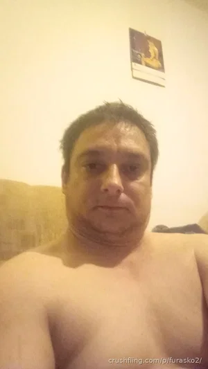 Shirtless man with short dark hair sitting indoors, facing camera.