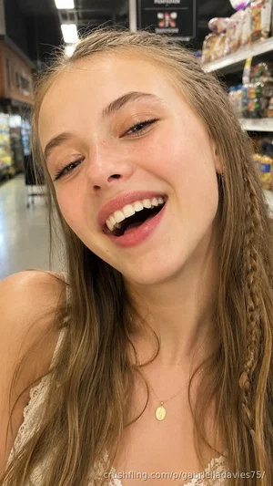 Woman with long braided hair, smiling, wearing lace top in grocery store aisle.