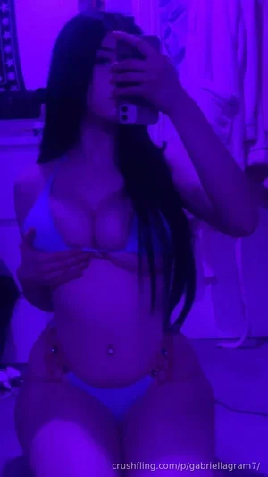 Woman in light blue lingerie taking mirror selfie under purple lighting.