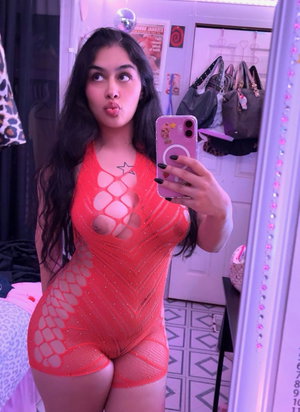 Woman in orange mesh bodysuit taking mirror selfie indoors.