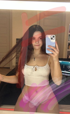 Brunette woman taking mirror selfie in white crop top and pink underwear.