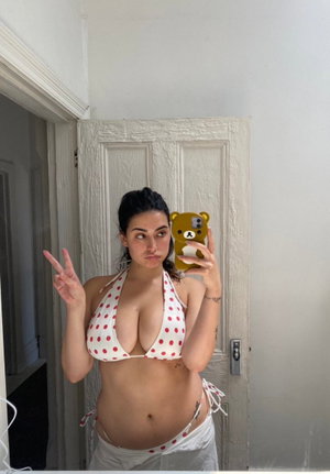 Woman in white polka-dot bikini taking mirror selfie in bedroom.