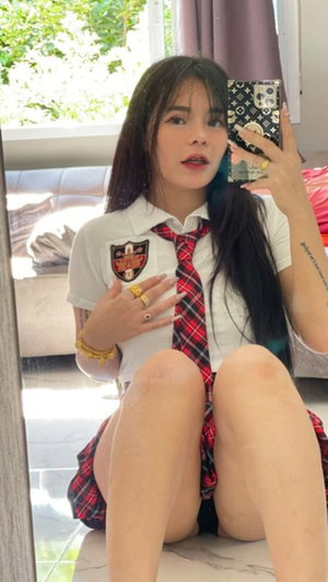 Asian woman in school uniform taking mirror selfie indoors.