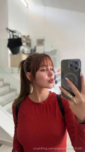 Woman in red long-sleeve top taking mirror selfie indoors, pouting lips, backpack straps visible.