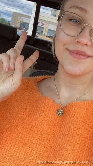 Woman with glasses in orange sweater making peace sign inside car.