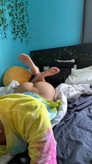 Curvy woman on bed in tie-dye shirt, bare buttocks, bedroom.