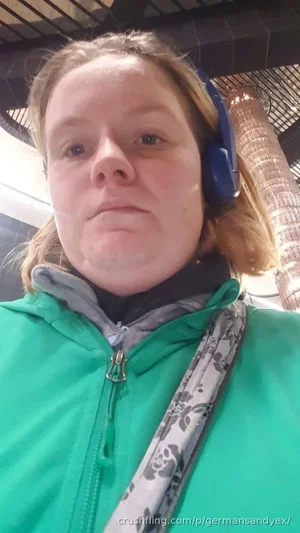 Woman in green jacket and blue headphones, indoor setting, looking at camera.