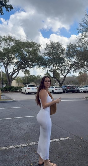 Woman in white dress posing outdoors in parking lot.
