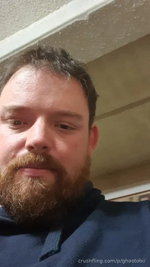 Man with beard and dark hair wearing a blue hoodie indoors.
