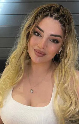 Blonde woman with braids in white tank top indoors.