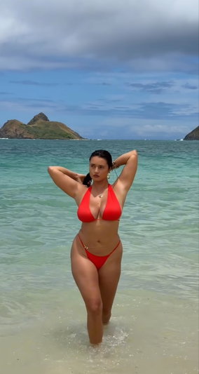 Woman in red bikini standing in shallow ocean water at beach.