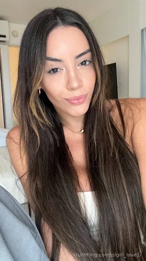 Woman with long dark hair and highlights, wearing a white top, indoors.
