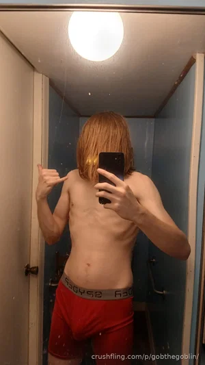 Shirtless man with red hair in red underwear taking mirror selfie in bathroom.