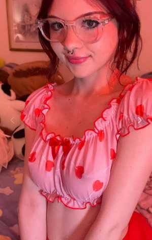 Redhead woman with glasses in pink heart top indoors.