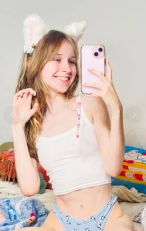 Blonde woman with cat ears taking a selfie in bedroom.