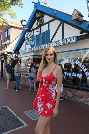Blonde woman in red floral dress outside bakery.
