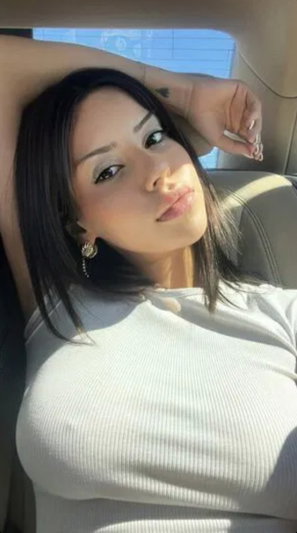 Dark-haired woman in white top reclining in car.