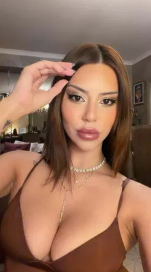 Brunette woman in brown top taking indoor selfie.