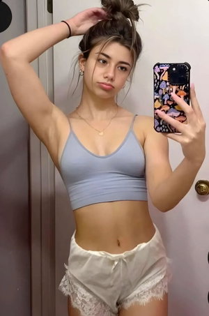 Woman in blue crop top and white shorts taking mirror selfie indoors.