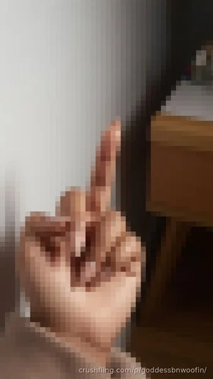 Hand making middle finger gesture indoors, blurred background with furniture.