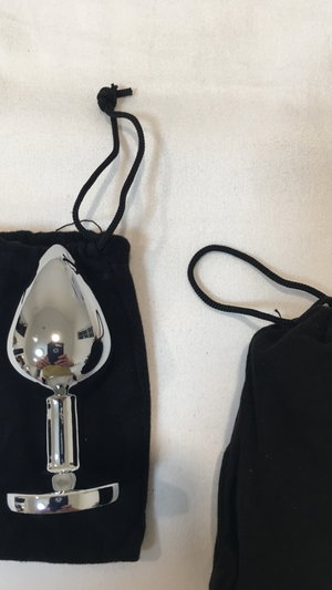 Steel butt plug with pouch on white sheet.