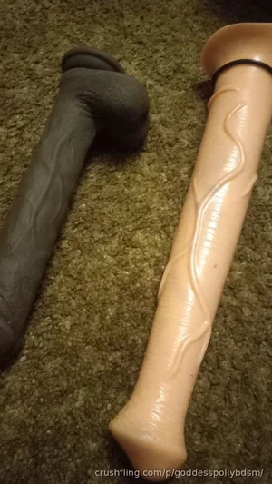 Two adult sex toys on a carpeted floor, one dark gray, one flesh-toned with textured design.