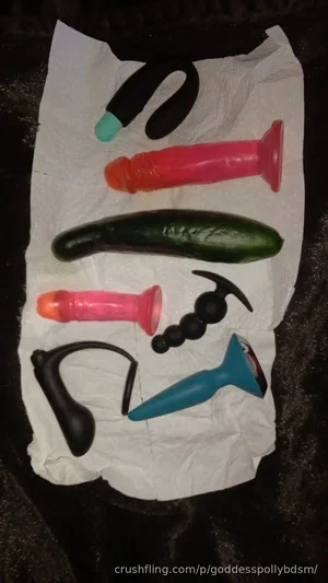 Various sex toys and a cucumber arranged on a white paper towel on a dark surface.
