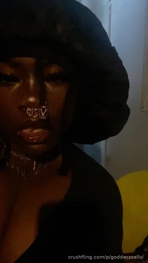 Woman with dark skin, black hat, lip jewelry, wearing black top indoors.