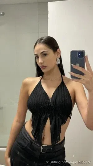 Woman in black halter top and pants taking mirror selfie in bathroom.