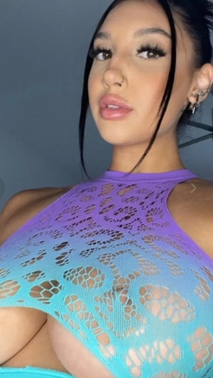 Dark-haired woman in colorful mesh top taking close-up selfie.