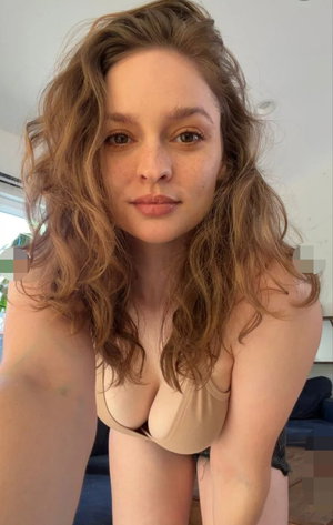 Curvy woman with wavy brown hair in beige bra taking indoor selfie.