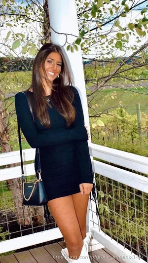 Woman in black dress and white boots standing on wooden deck outdoors.