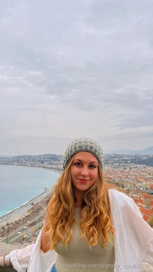 Woman with long blonde hair wearing a beanie and light top, standing on a hill overlooking a