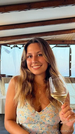 Woman with long wavy hair in floral top holding wine glass, smiling indoors.