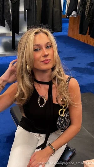 Blonde woman in black top and white pants sitting in a clothing store.