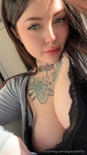 Woman with dark hair and tattoos, wearing black lace top and gray cardigan, indoors.