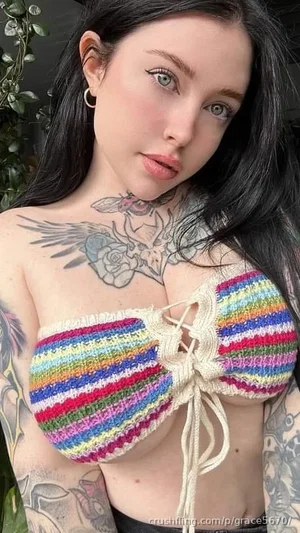 Woman with dark hair and tattoos wears colorful knitted top, indoors.