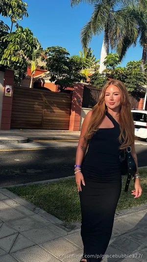 Woman in black halter dress standing outdoors on sidewalk near palm trees.
