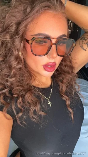 Woman with curly hair, sunglasses, and black top posing indoors.